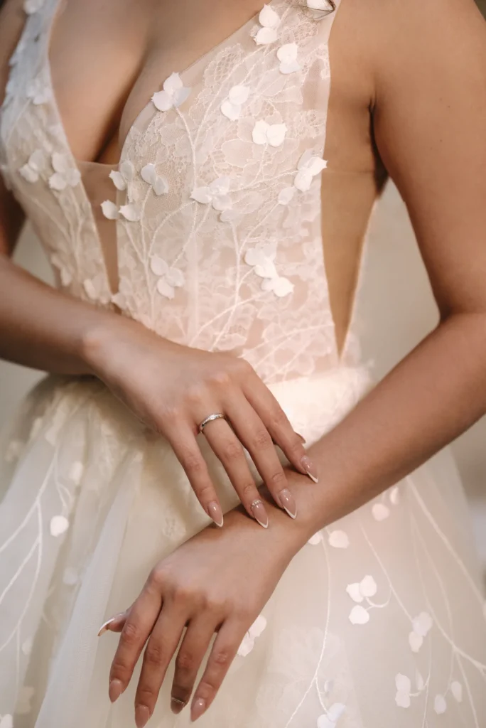 Közelkép csipkés menyasszonyi ruha felsőrészéről és a menyasszony kezén lévő gyűrűről