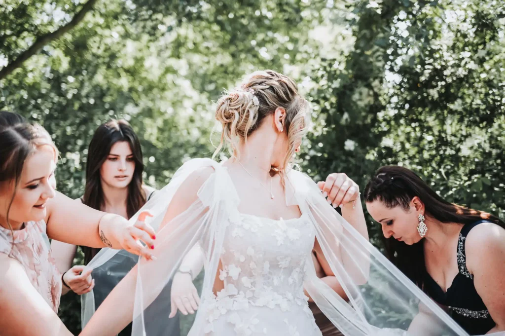 Barátnők segítenek a menyasszonynak a fátyol beállításában szabadtéri környezetben